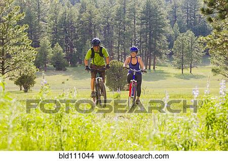 Couple riding mountain bikes in meadow View Large Photo Image Picture - Couple riding mountain bikes in meadow. Fotosearch