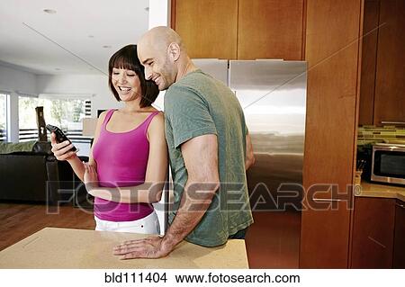 Picture - Couple using cell phone in kitchen. Fotosearch
