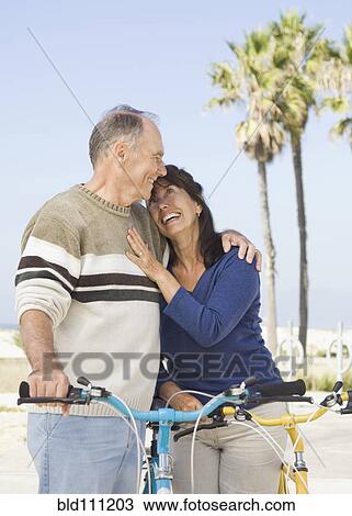 Stock Image - Couple walking bicycles on beach. Fotosearch