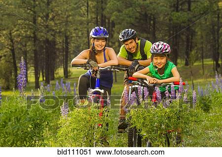 Stock Image - Family sitting on bicycles in meadow. Fotosearch