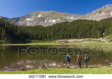 Stock Image - Hikers admiring still lake in rural landscape. Fotosearch