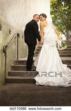 Stock Photograph - Hispanic bride and groom walking up steps. Fotosearch