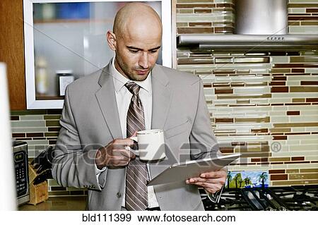 Stock Photo - Hispanic businessman using tablet computer in kitchen. Fotosearch