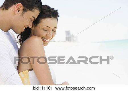 Stock Image - Hispanic couple hugging on beach. Fotosearch