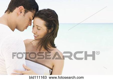 Stock Image - Hispanic couple hugging on beach. Fotosearch