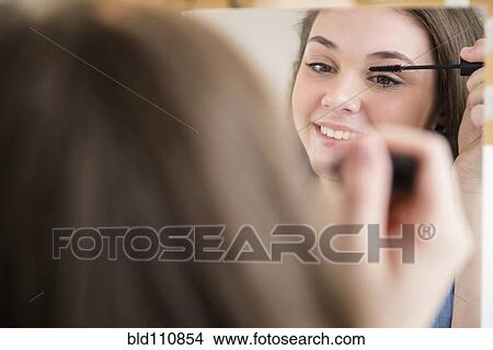 Picture - Hispanic girl applying makeup in mirror. Fotosearch