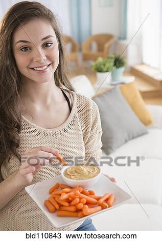 Stock Image - Hispanic girl eating carrots and hummus. Fotosearch