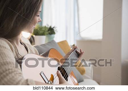 Hispanic girl playing guitar on sofa View Large Photo Image Picture - Hispanic girl playing guitar on sofa. Fotosearch