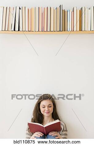 Stock Photography - Hispanic girl reading under bookshelf. Fotosearch