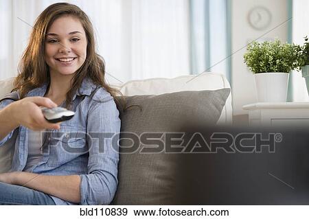 Stock Photo - Hispanic girl watching television on sofa. Fotosearch