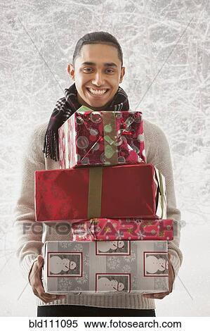 Stock Photography - Hispanic man holding stack of presents in snow. Fotosearch