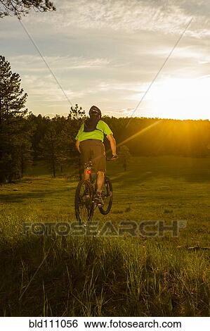 Stock Photograph - Hispanic man riding mountain bike in meadow. Fotosearch