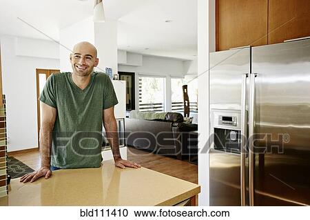 Stock Image - Hispanic man standing in kitchen. Fotosearch