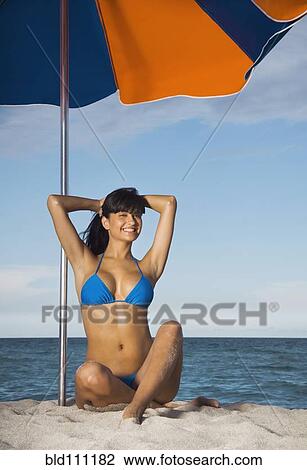 Stock Image - Hispanic woman in bikini under beach umbrella. Fotosearch