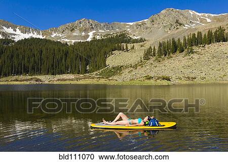 Stock Image - Hispanic woman laying on paddle board. Fotosearch