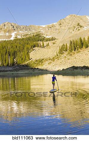 Stock Image - Hispanic woman riding paddle board. Fotosearch