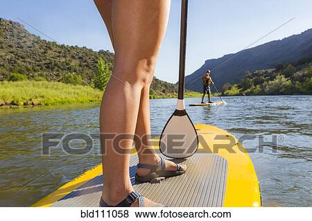 Stock Photo - Hispanic woman riding paddle board. Fotosearch