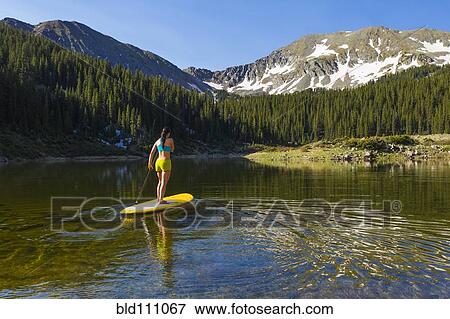 Stock Photo - Hispanic woman riding paddle board. Fotosearch