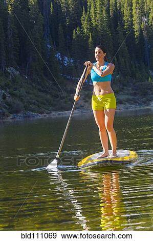 Stock Photo - Hispanic woman riding paddle board. Fotosearch