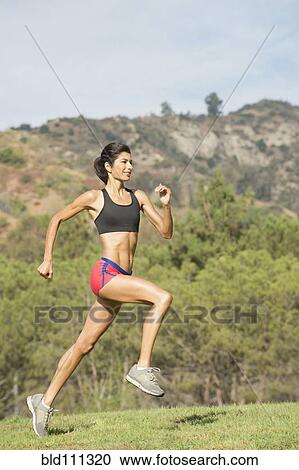 Stock Image - Hispanic woman running in rural field. Fotosearch