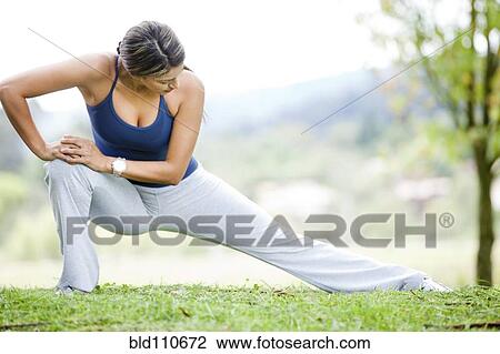 Stock Image - Hispanic woman stretching in grass. Fotosearch