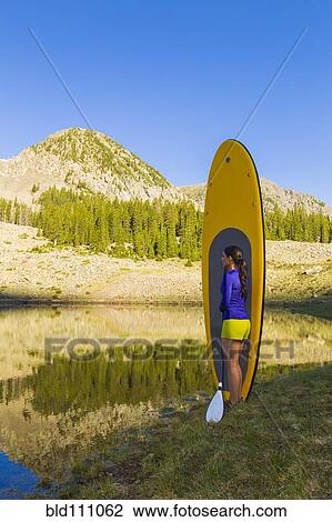 Stock Image - Hispanic woman with paddle board in rural landscape. Fotosearch