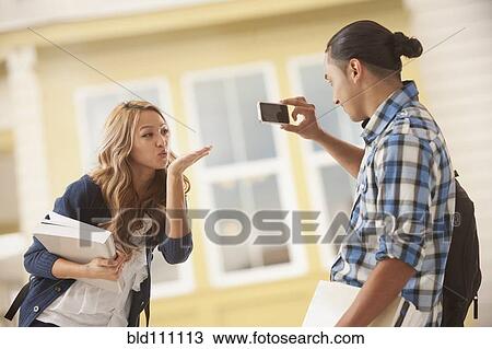 Stock Image - Man taking picture of girlfriend blowing kiss. Fotosearch