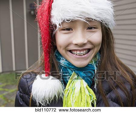 Stock Image - Mixed race girl in braces wearing Santa hat. Fotosearch