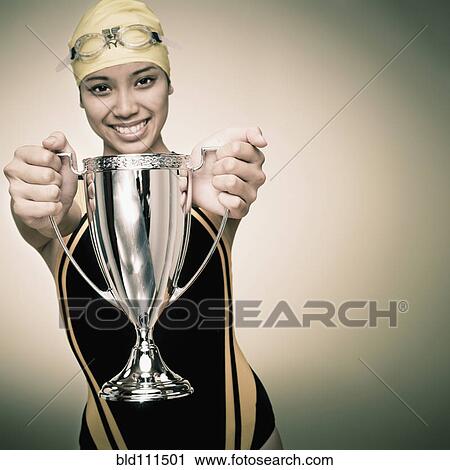 Stock Image - Mixed race swimmer holding trophy. Fotosearch