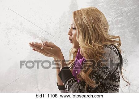 Stock Photo - Mixed race woman blowing handful of snow. Fotosearch