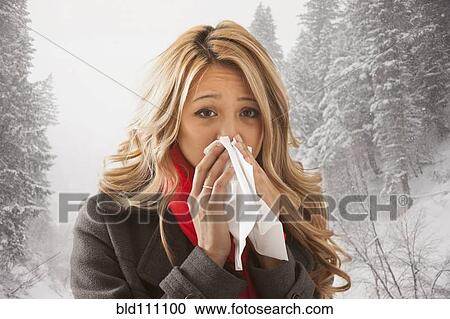 Stock Image - Mixed race woman blowing her nose in snow. Fotosearch