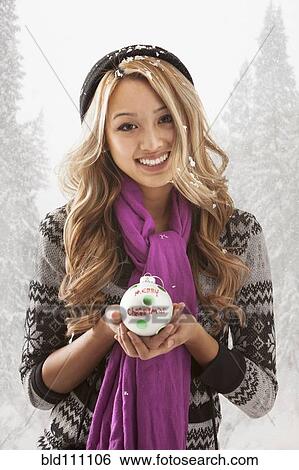 Stock Photograph - Mixed race woman holding Christmas ornament in snow. Fotosearch