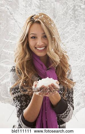 Stock Image - Mixed race woman holding handful of snow. Fotosearch