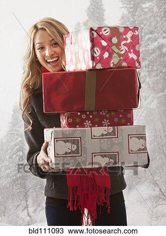 Stock Image - Mixed race woman holding stack of presents in snow. Fotosearch