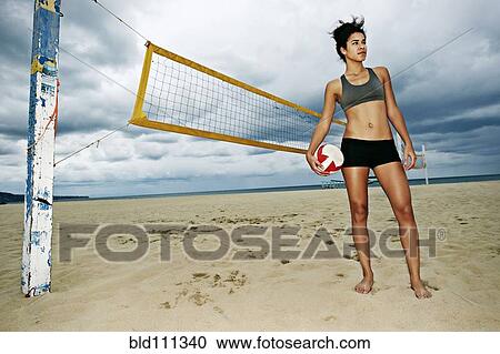 Stock Image - Mixed race woman holding volleyball on beach. Fotosearch