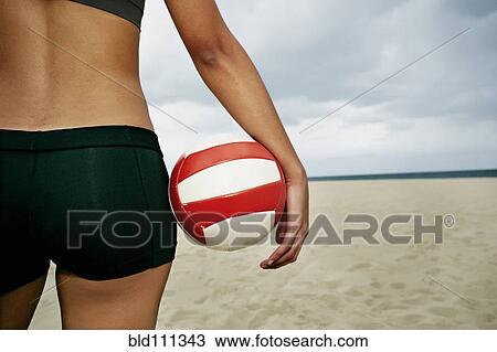 Stock Image - Mixed race woman holding volleyball on beach. Fotosearch