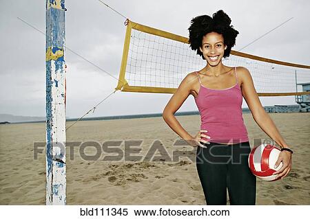 Stock Photography - Mixed race woman holding volleyball on beach. Fotosearch