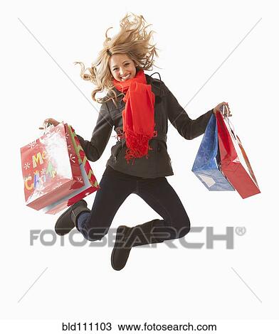 Stock Image - Mixed race woman jumping with shopping bags. Fotosearch