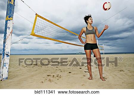 Stock Image - Mixed race woman playing with volleyball on beach. Fotosearch