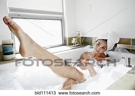 Stock Image - Mixed race woman shaving in bubble bath. Fotosearch