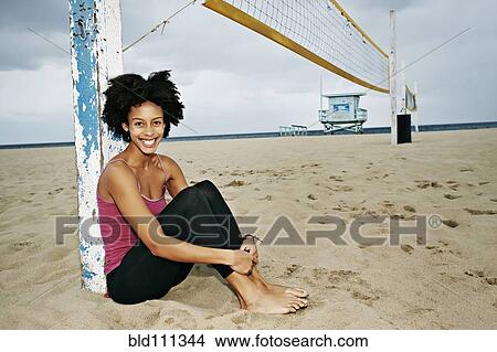 Picture - Mixed race woman sitting by volleyball net on beach. Fotosearch