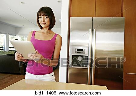 Stock Photograph - Mixed race woman using tablet computer in kitchen. Fotosearch