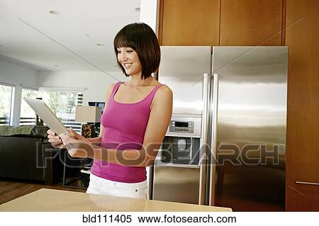 Stock Photography - Mixed race woman using tablet computer in kitchen. Fotosearch