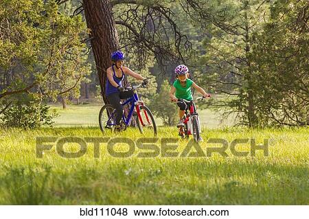 Stock Photo - Mother and daughter riding mountain bikes in meadow. Fotosearch