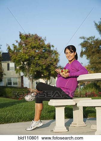Stock Image - Pregnant Hispanic woman eating fruit salad. Fotosearch