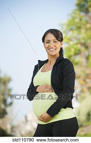 Stock Image - Pregnant Hispanic woman holding her belly outdoors. Fotosearch