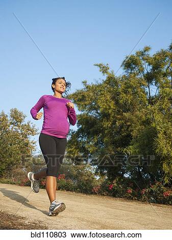 Stock Image - Pregnant Hispanic woman jogging outdoors. Fotosearch