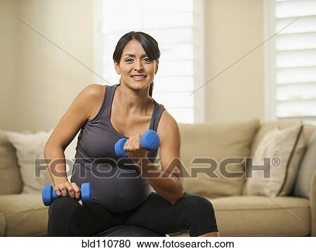 Stock Image - Pregnant Hispanic woman lifting weights. Fotosearch
