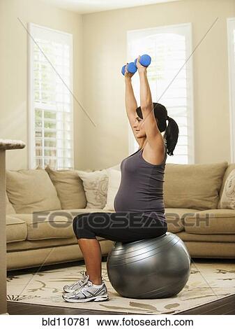 Stock Image - Pregnant Hispanic woman lifting weights. Fotosearch