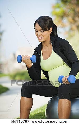 Stock Photo - Pregnant Hispanic woman lifting weights outdoors. Fotosearch